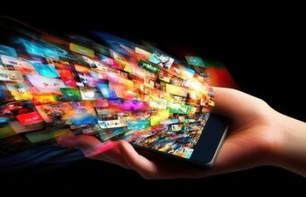La inversión publicitaria digital en Europa alcanza máximos históricos a costa de sobrecargar a las plantillas Una mano sostiene un teléfono móvil del que emergen numerosas imágenes que representan el crecimiento exponencial de la publicidad digital y la constante exposición de los usuarios a contenidos.