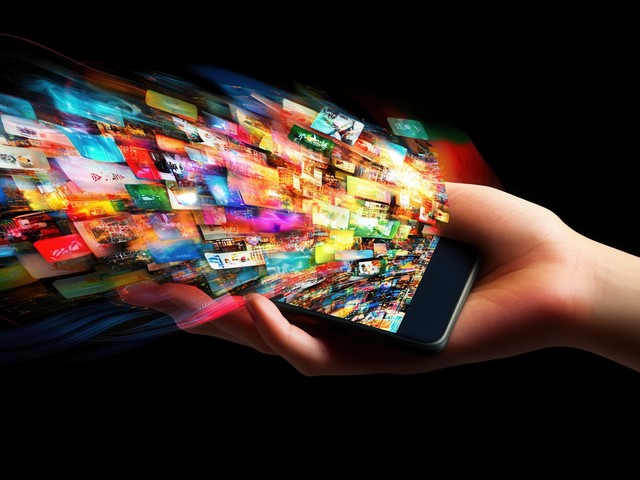 Publicidad_Digital Una mano sostiene un teléfono móvil del que emergen numerosas imágenes que representan el crecimiento exponencial de la publicidad digital y la constante exposición de los usuarios a contenidos.