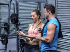 Los usuarios de instalaciones deportivas priorizan la salud y la atención personalizada Mujer y hombre conversando junto a una máquina de pesas en un gimnasio mientras revisan una tabla de entrenamiento.