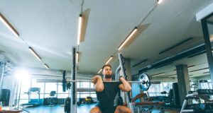 Hombre levantando una barra con pesas durante un entrenamiento en un establecimiento que pertenece a una cadena de gimnasios.
