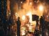 Rodaje cinematográfico con efectos especiales de explosiones y chispas, mientras el equipo técnico trabaja entre cámaras, focos y medidas de seguridad en un set de filmación nocturno.