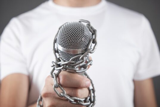 La Agrupación de Periodistas de UGT rechaza la expulsión de los equipos de RTVE y EFE de Castillejos y exige garantías para el libre ejercicio del periodismo Mano que sostiene un micrófono encadenado, símbolo de las restricciones al libre ejercicio del periodismo tras la expulsión de RTVE y EFE de Castillejos.