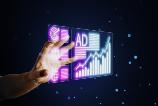 Meta cobra por anuncios ilícitos y evidencia el fracaso de los filtros automáticos Mano interactuando con un panel digital de publicidad y gráficos, en referencia a los anuncios ilícitos de Meta y al fracaso de sus filtros automáticos.