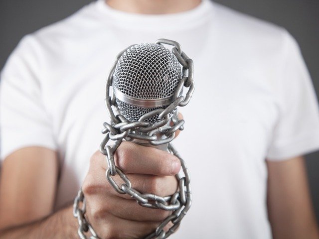Mano que sostiene un micrófono encadenado, símbolo de las restricciones al libre ejercicio del periodismo tras la expulsión de RTVE y EFE de Castillejos.