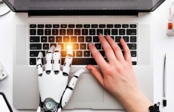 UGT Cultura se adhiere al manifiesto internacional que reclama actuar ante el impacto laboral de la IA Impacto laboral de la IA representado por una mano humana y una mano robótica trabajando juntas sobre el teclado de un ordenador portátil.