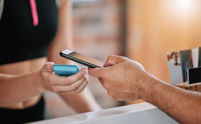 Persona pagando con el móvil una cuota de gimnasio mediante un terminal electrónico.