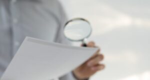 Una persona examina unos documentos con una lupa, en referencia al análisis del decreto sobre grupos de interés y su impacto en la negociación colectiva.