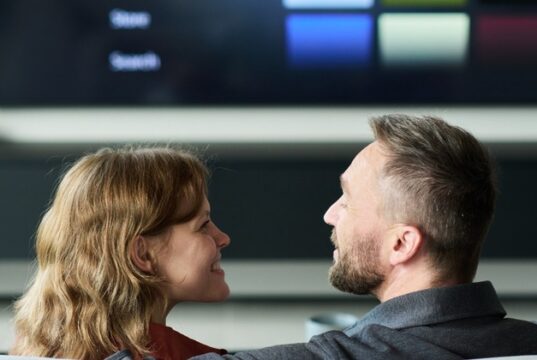 Pareja frente a un televisor inteligente con un menú de contenidos audiovisuales.