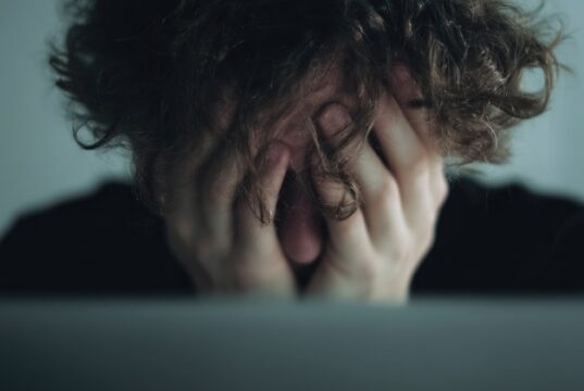 Estrés postvacacional: cuándo la vuelta al trabajo afecta a tu salud Persona abrumada oculta el rostro entre las manos en una imagen que refleja estrés y agotamiento emocional.