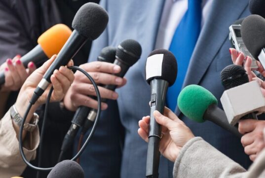Varios periodistas acercan sus micrófonos a un portavoz, una imagen que ilustra la polémica por la clasificación ideológica de profesionales de la información elaborada por Interior.