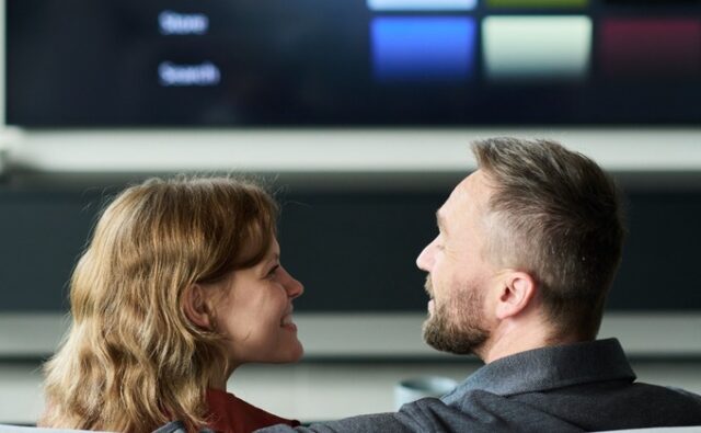 watching-tv-together-living-room-680x420 Pareja frente a un televisor inteligente con un menú de contenidos audiovisuales.