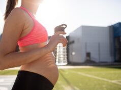Mujer embarazada con ropa deportiva y botella de agua durante un entrenamiento.