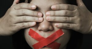 Mujer con los ojos cubiertos por sus manos y la boca sellada con cinta adhesiva roja, que simboliza la censura a la que se opone UGT Cultura.