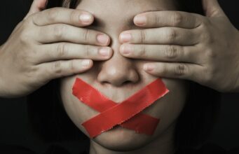 Mujer con los ojos cubiertos por sus manos y la boca sellada con cinta adhesiva roja, que simboliza la censura a la que se opone UGT Cultura.