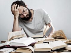 La seguridad laboral también importa en la cultura Trabajador con gesto de agotamiento entre libros, imagen que ilustra el estrés y los riesgos psicosociales en el trabajo.