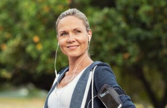 Trabajar en el deporte después de los 45: una carrera sin red Mujer adulta con ropa deportiva y auriculares durante un entrenamiento al aire libre, en una noticia sobre la continuidad laboral en gimnasios después de los 45 años.