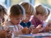 La UE propone limitar las redes sociales a menores y frenar su diseño adictivo Niños consultan sus teléfonos móviles en una mesa escolar, una escena relacionada con la propuesta europea para proteger a los menores en Internet.