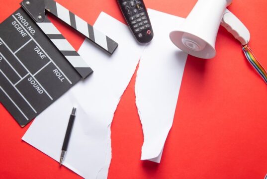 Claqueta, mando de televisión y megáfono sobre documentos rotos, imagen de los recortes de empleo y la reestructuración en el sector audiovisual.