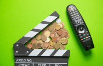 El sector audiovisual alerta del recorte del 30% en AgoraEU Claqueta de cine junto a monedas y un mando a distancia, en referencia a los recortes y la financiación del sector audiovisual.