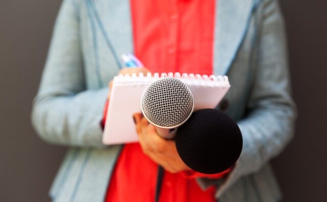 midsection-journalist-microphones-680x420 Periodista tomando notas con micrófonos en la mano.